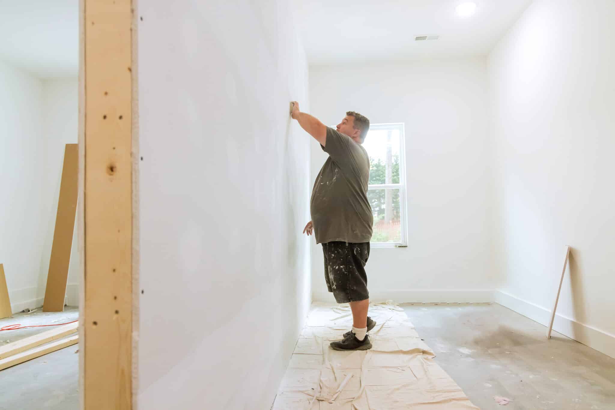 as the work is being carried out on the renovation of the house in the room, a worker is using the sand trowel to sand the drywall mud with