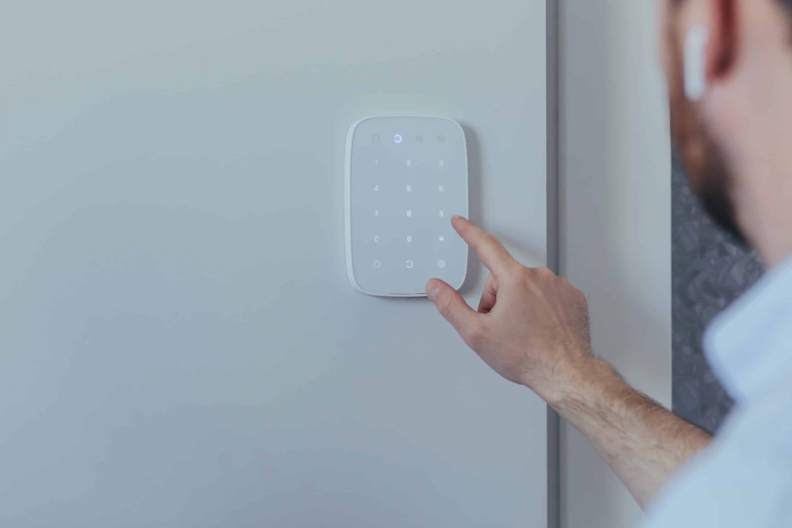 businessman enters finger password lock code on alarm panel, on white wall