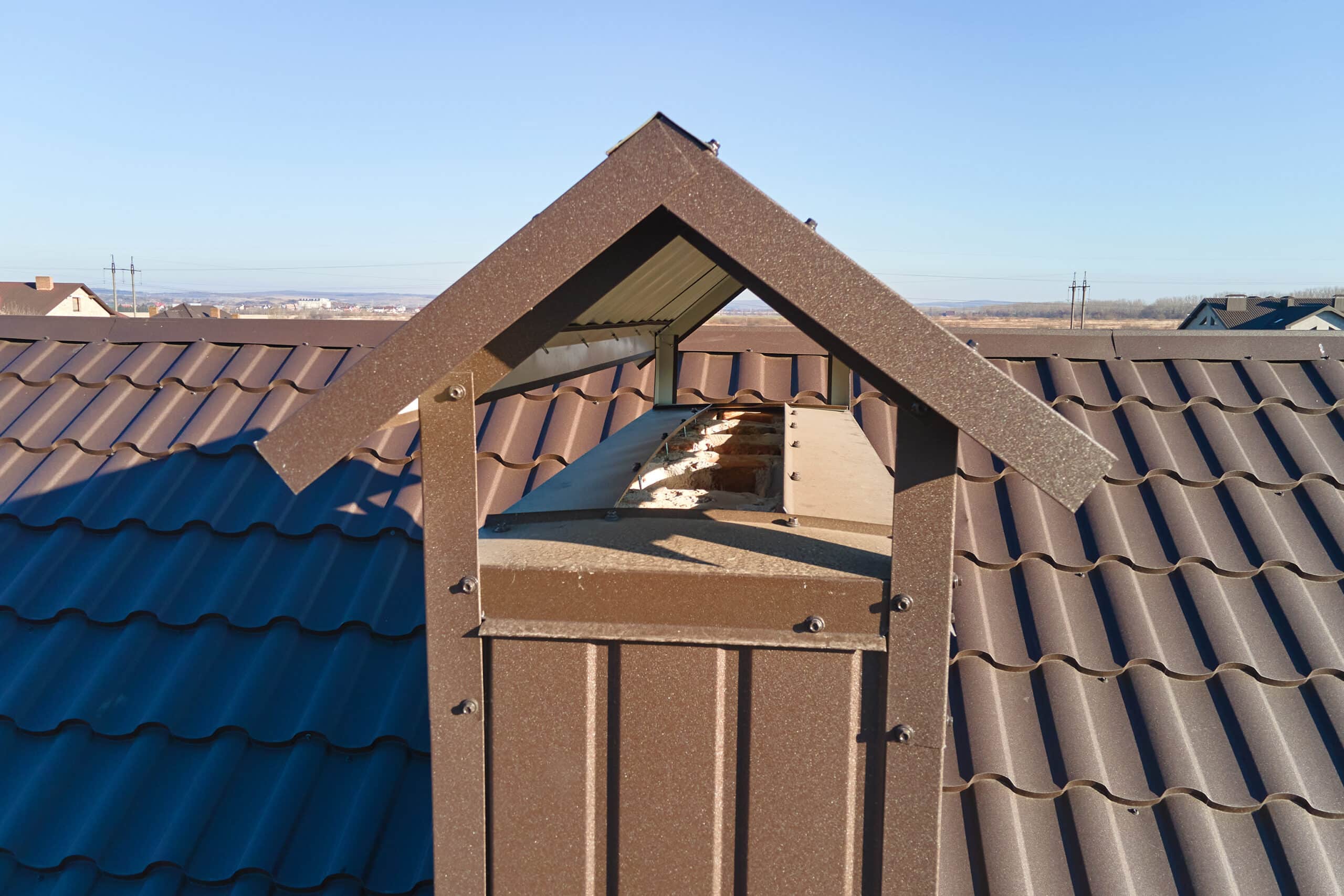 chimney on house roof top covered with metallic shingles under construction. tiled covering of building. real estate development