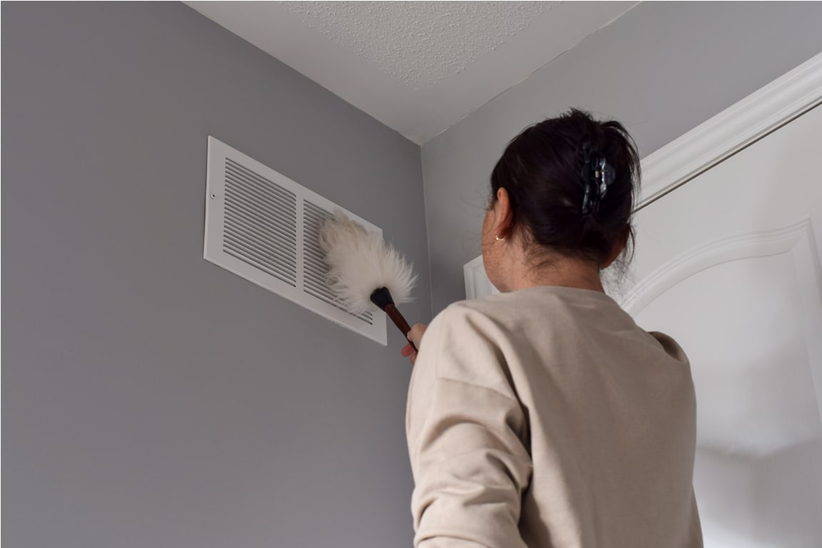 woman cleaning return air vent with duster