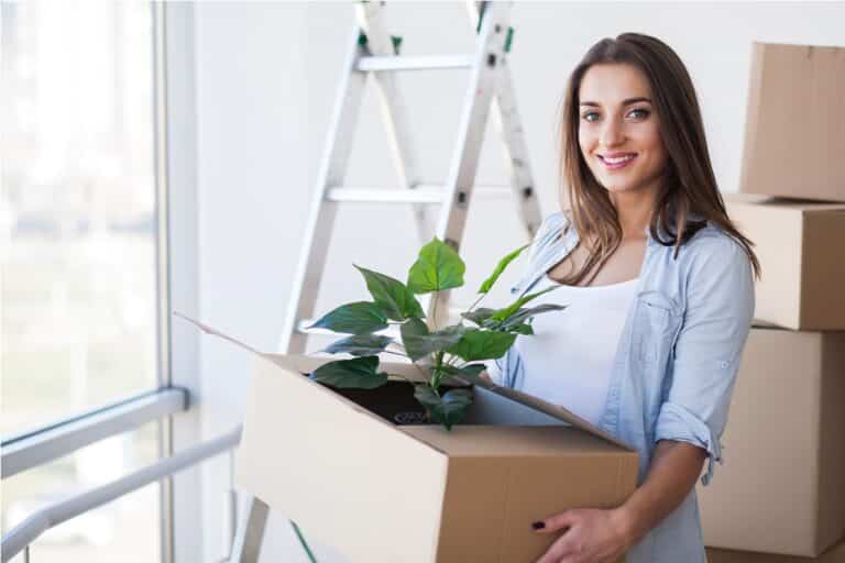 happy young adult woman holding moving boxes in empty room in a new house.
