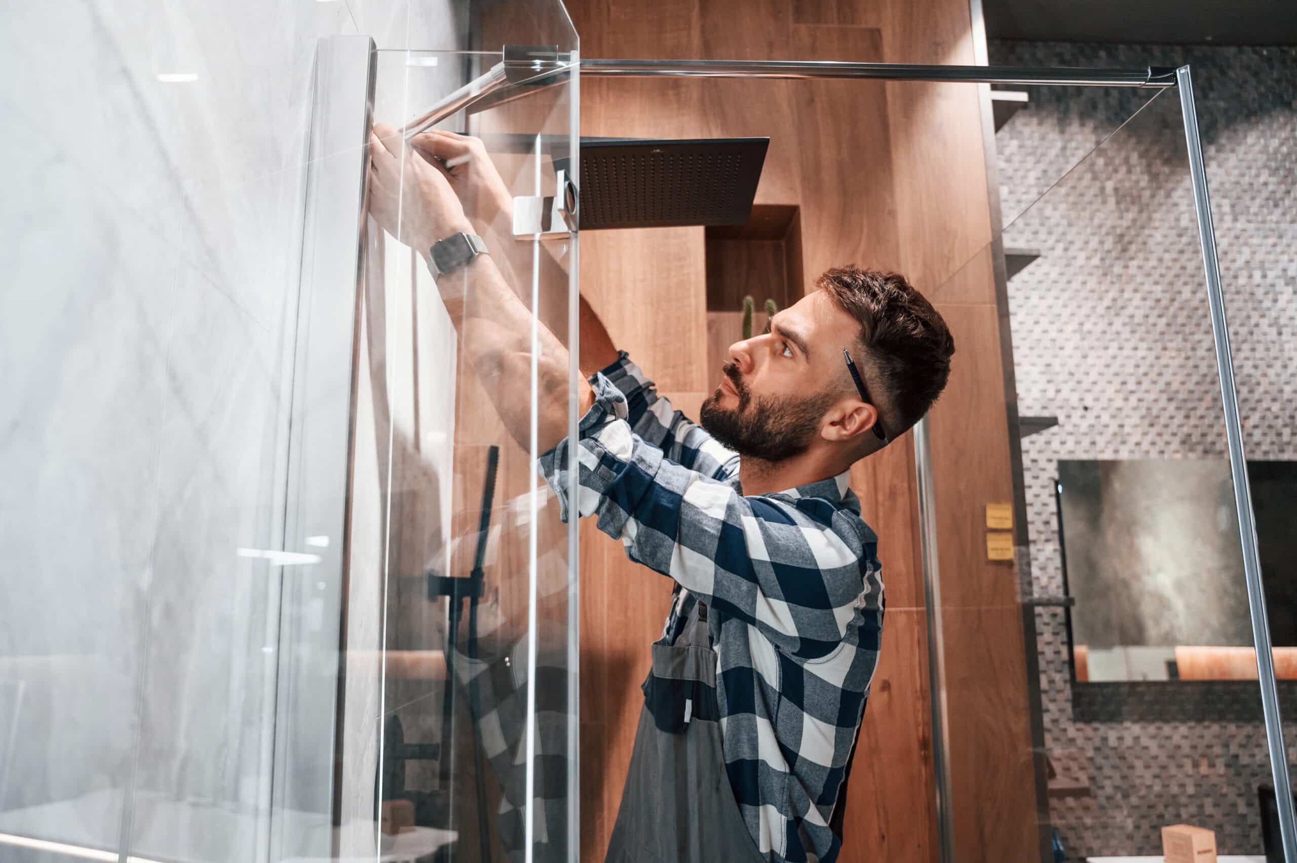 repairs the shower cabin. plumber in uniform is indoors at home