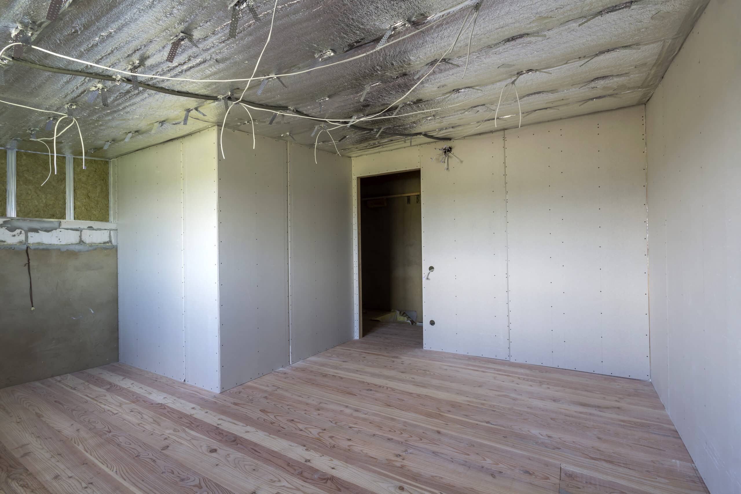 room under construction with silver aluminum insulation foil and drywall on walls and ceiling.
