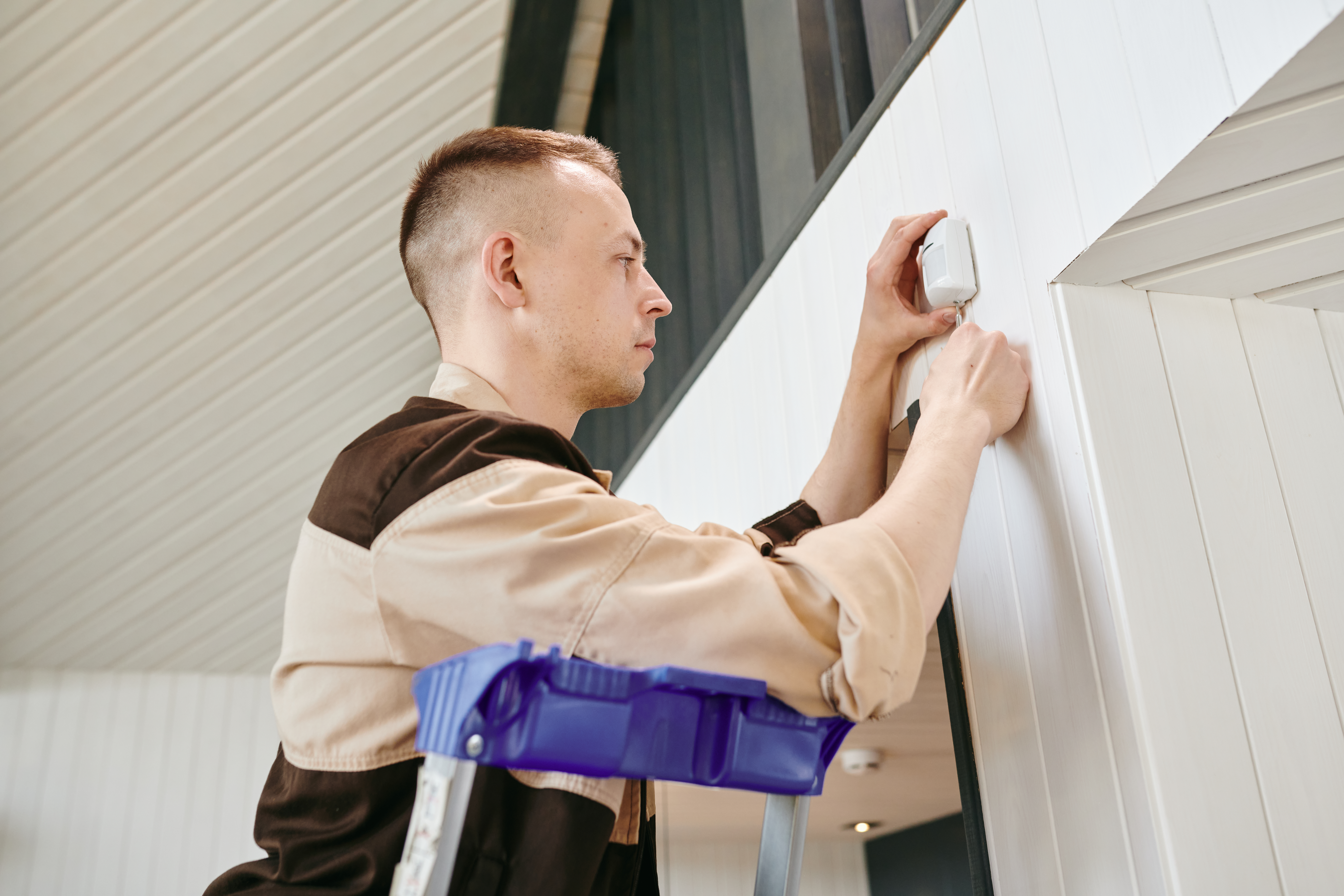 young man in uniform putting alarm system on wall