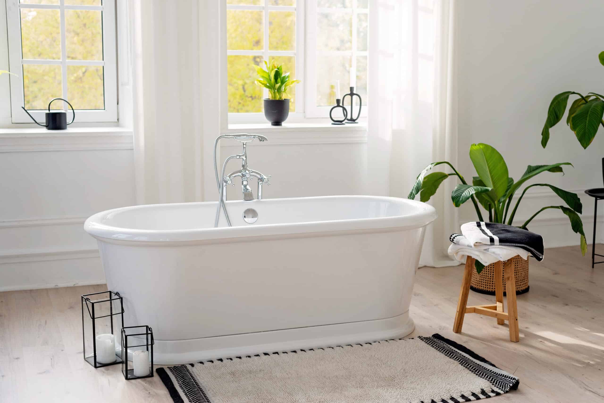 stylish modern bathroom interior. horizontal view of an empty free standing bathtub on a wooden floor in a bright room against the backdrop of a large window and houseplants. soft selective focus.