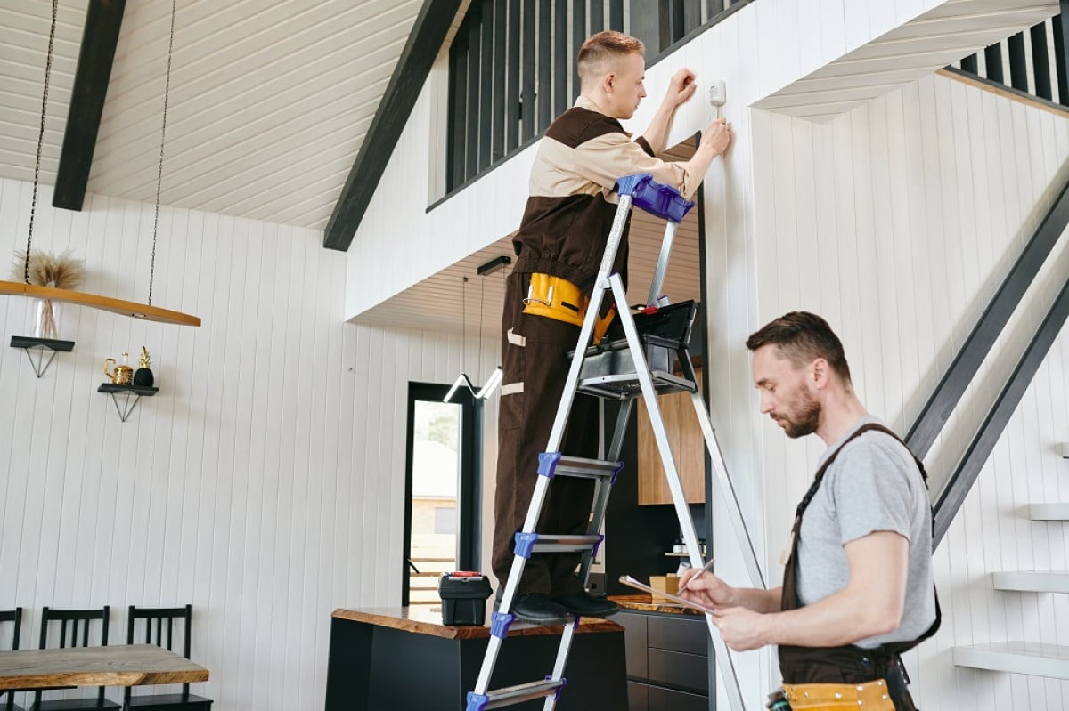 deux professionnels fixant un systeme dalarme dans le salon