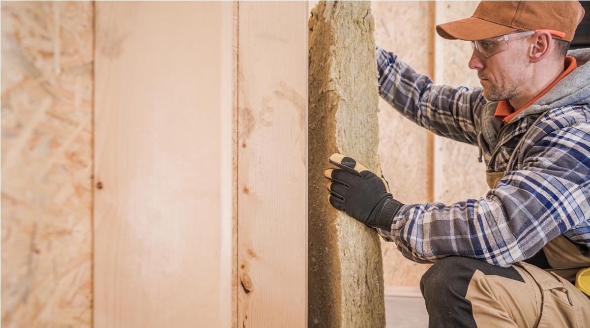 worker insulating house walls with piece of mineral wool
