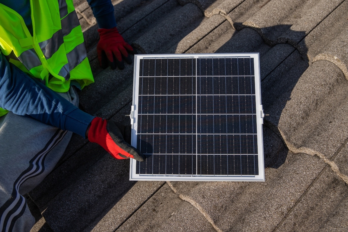 a technician installs a photovoltaic solar panel on a roof, sustainable energy