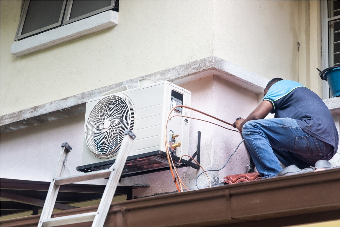 technician installing outdoor air conditioner compressor unit on outdoor wall