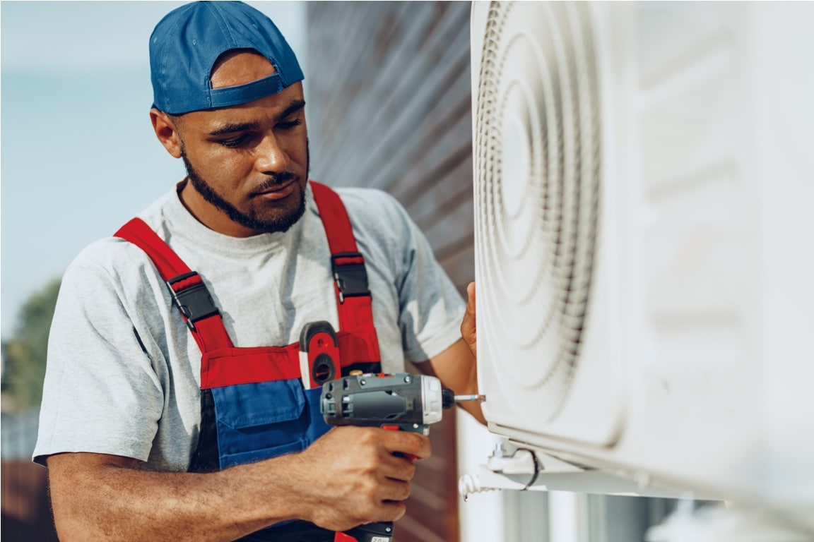 repairman in uniform installing the outside unit of air conditioner