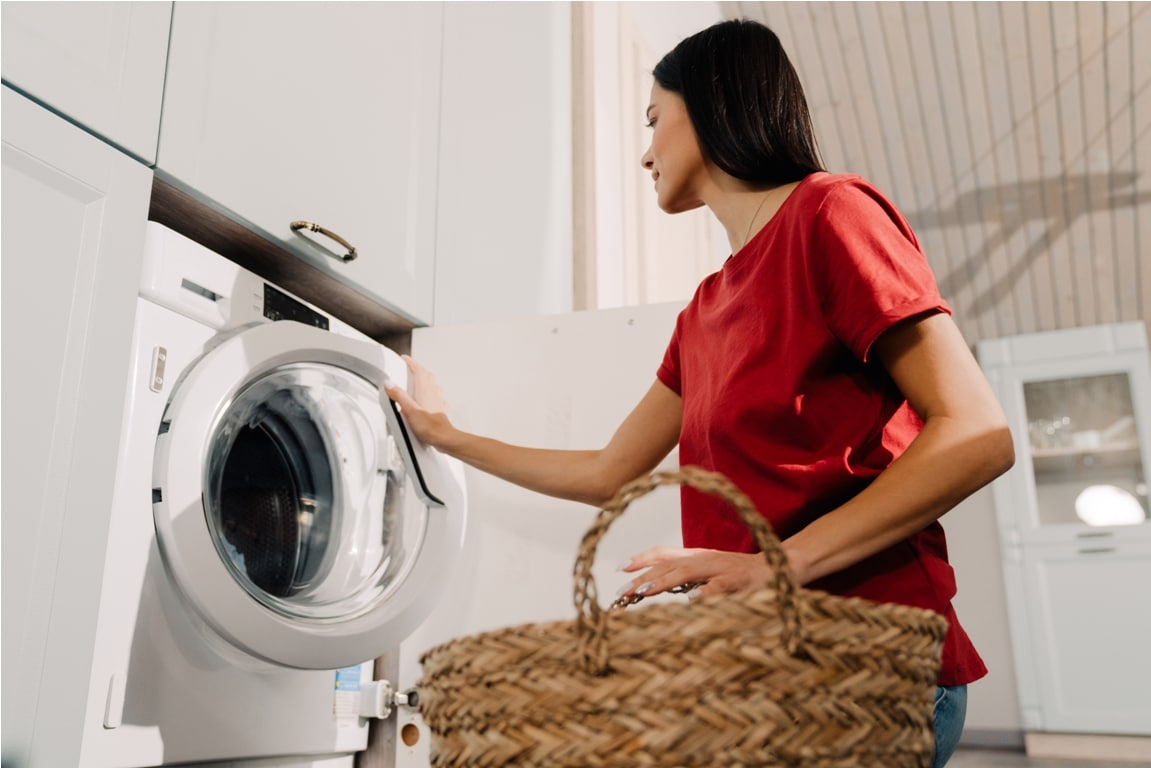 young woman putting clothes at washing machine while doing laundry
